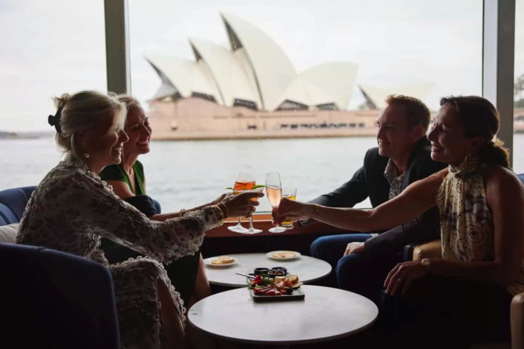 실내에 앉아 음료와 함께 토스트를 즐기는 두 명의 여성은 뒤쪽 창문을 통해 시드니 오페라하우스의 전망을 감상할 수 있습니다.