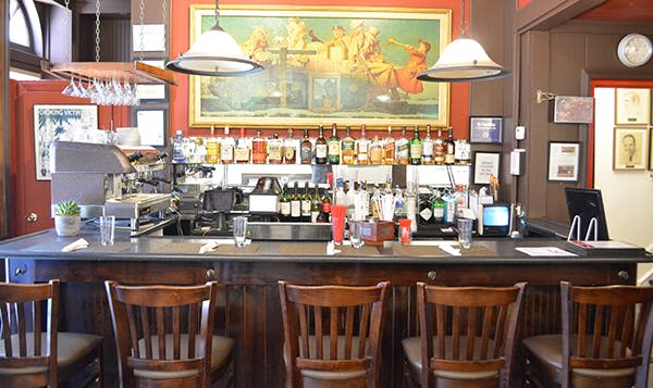 나무 스툴이 있는 바, 카운터 뒤에는 다양한 병에 담긴 음료, 벽에는 르네상스 시대의 대형 그림이 있습니다.