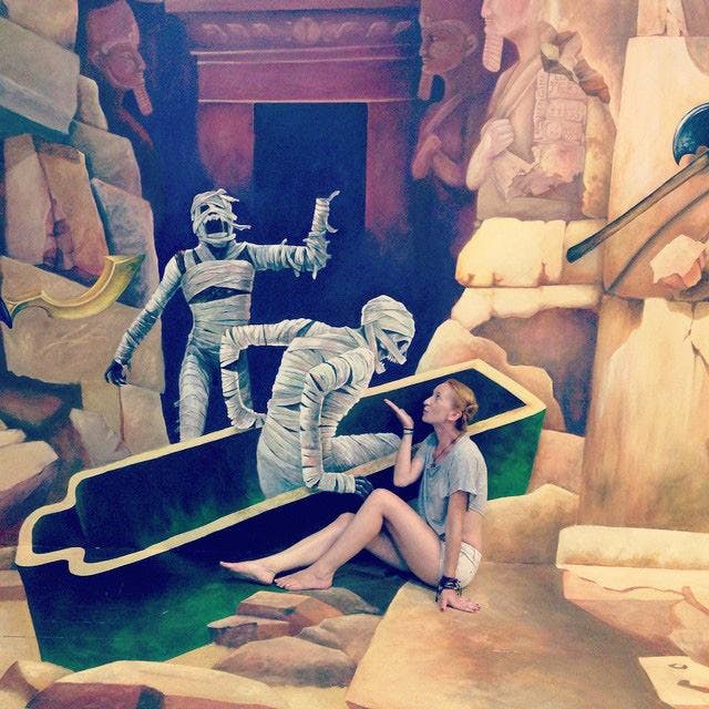 고대 이집트 풍의 석관에서 나온 두 미라의 벽화 앞에서 한 여성이 장난스럽게 포즈를 취하고 있습니다.