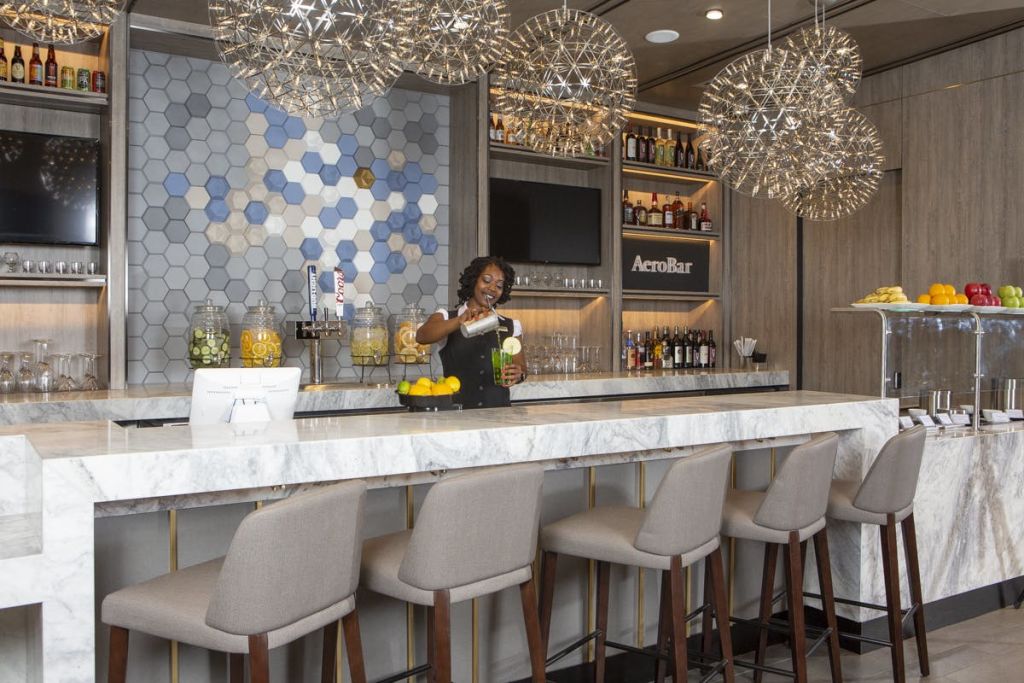 바텐더가 6각형 벽 타일과 장식 조명이 있는 현대적인 바의 대리석 카운터 뒤에서 음료를 믹스합니다.