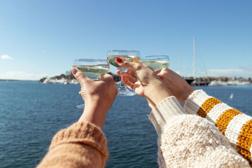 화창한 날씨에 아름다운 바닷가와 보트를 배경으로 토스트에 샴페인 잔을 들고 있는 세 손.