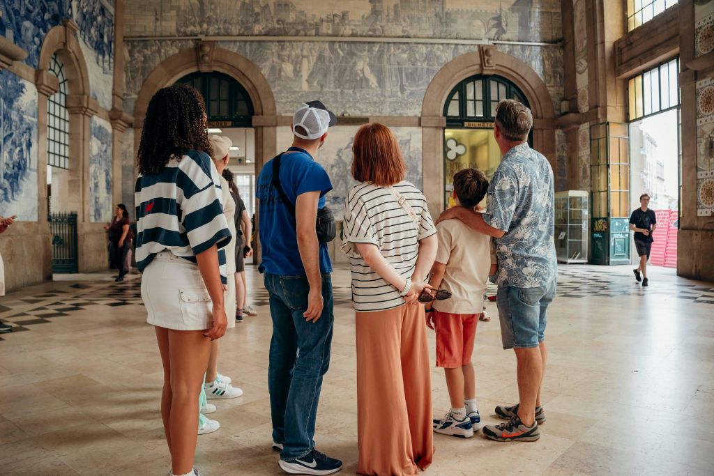 한 무리의 사람들이 아치형 창문과 체크무늬 바닥이 있는 건물 내부의 벽화를 마주하고 있습니다.