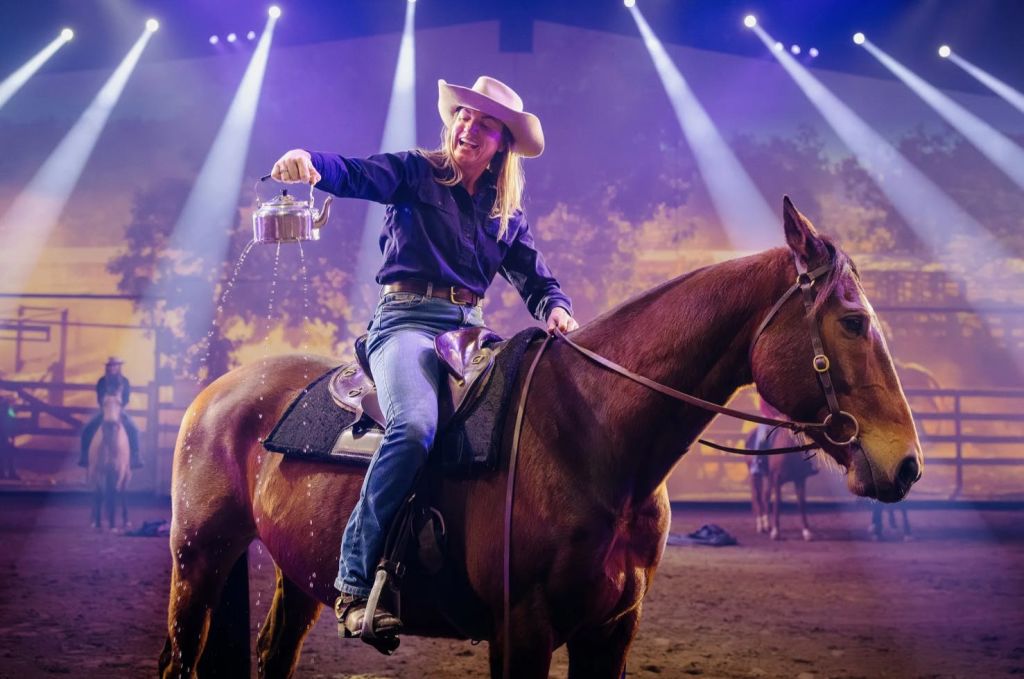 경치가 아름다운 무대 조명 아래에서 주전자에서 물을 붓고 말을 타고 있는 카우보이 모자를 쓴 사람.