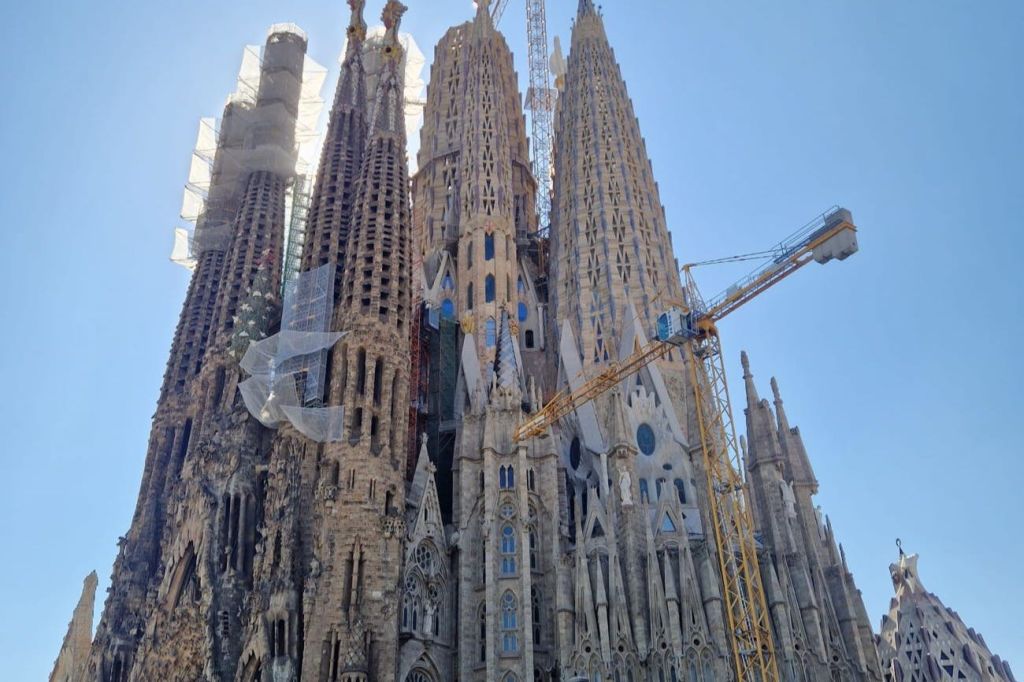 우뚝 솟은 첨탑이 지어진 고딕 양식의 교회로, 맑고 푸른 하늘을 배경으로 크레인과 비계가 특징입니다.