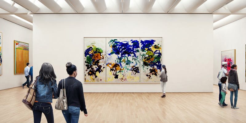 아트 갤러리에서 파란색, 녹색, 노란색, 검은색의 굵은 획이 있는 대형 추상 트리프티크 그림을 보는 두 사람.