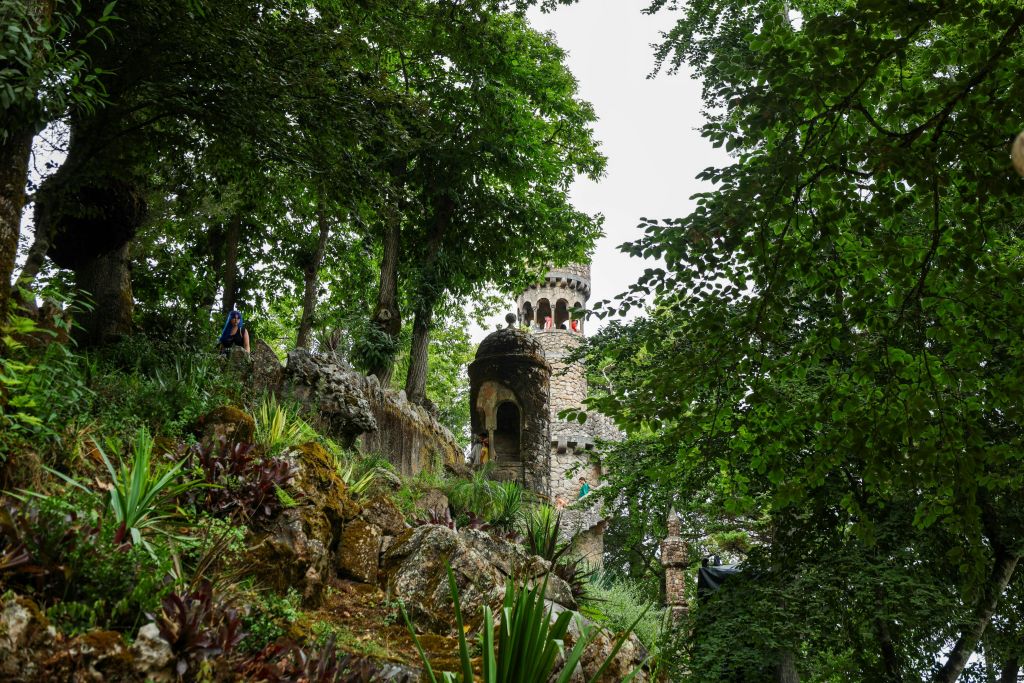 아치형 통로가 있는 석탑은 울창한 푸른 나무와 초목으로 인해 부분적으로 가려지며, 앞쪽에는 바위와 식물이 있습니다.