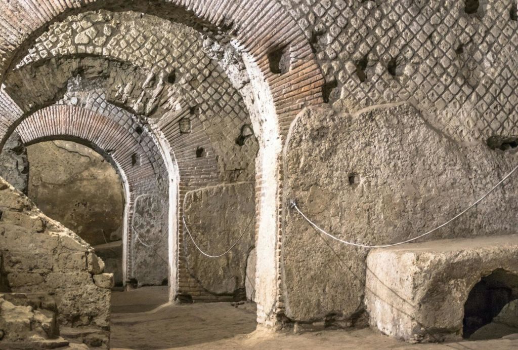 고대 돌과 벽돌로 장식된 아치형 통로로 로마식 디자인이 돋보이며, 질감이 살아있는 벽과 밧줄로 둘러싸여 있습니다.