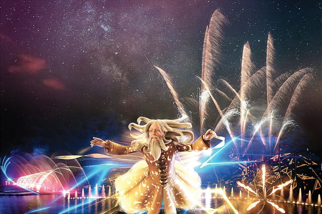 불꽃놀이와 별이 빛나는 하늘을 배경으로 흐르는 머리카락과 함께 빛나는 의상을 입은 수염이 있는 인물이 등장하는 환상적인 장면.