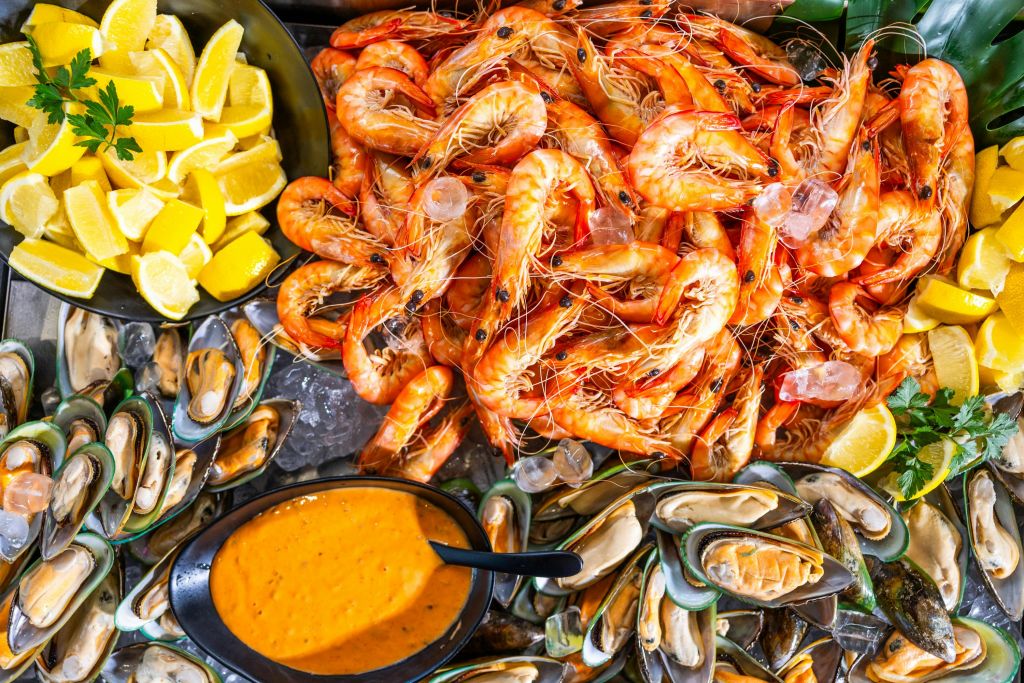 오렌지 디핑 소스 한 그릇에 새우, 홍합, 레몬 웨지 등 다양한 신선한 해산물이 준비되어 있습니다.