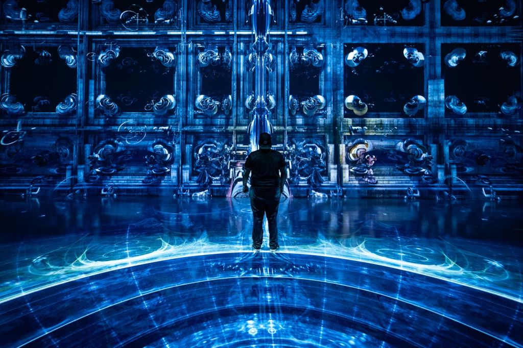 무대에서 활기찬 주황색 조명 아래에서 밴드가 배경에서 연주하는 모습으로 열정적으로 노래를 부르는 여성이 있습니다.