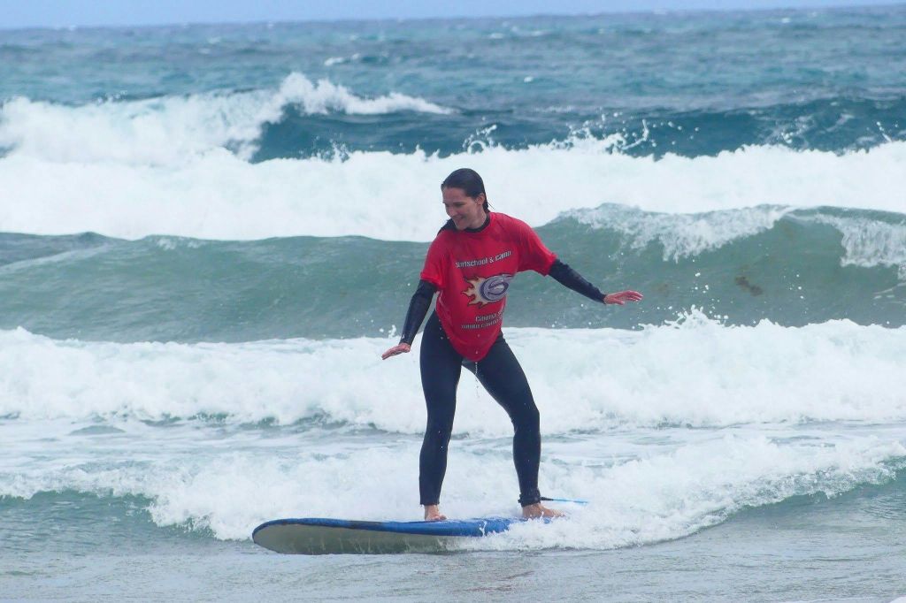 바다 파도 위에서 서핑보드를 타고 있는 빨간색 셔츠와 검은색 바지를 입은 사람.