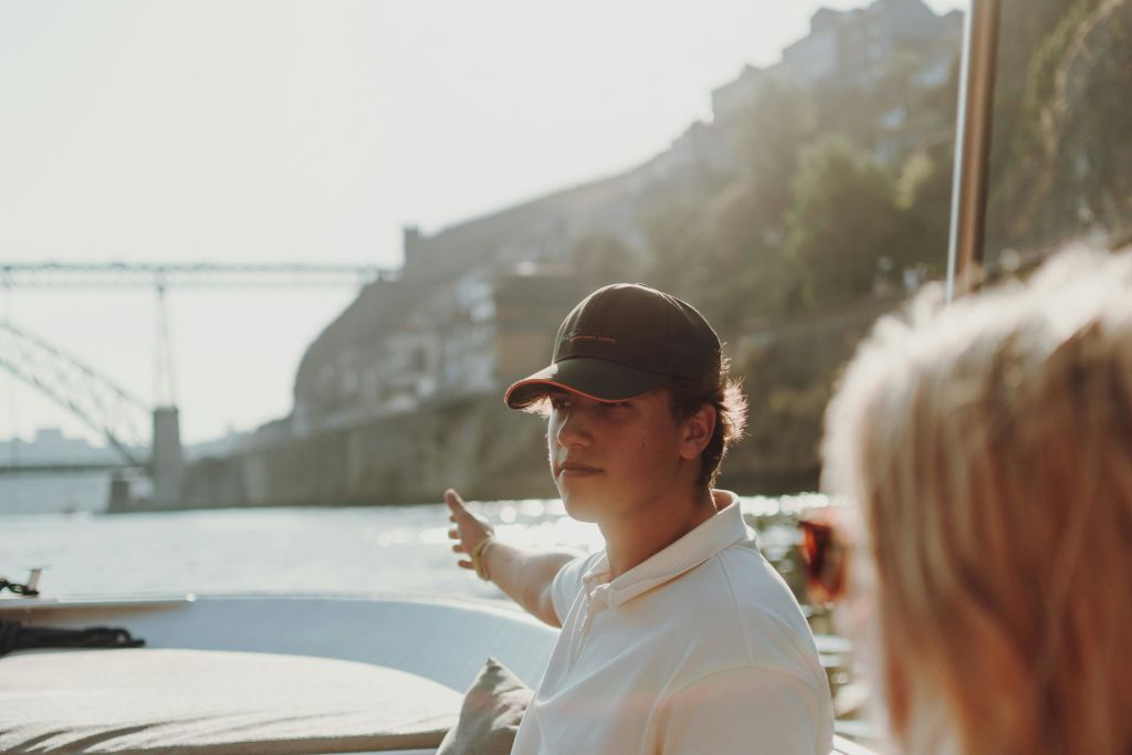 보트에서 보이는 것처럼 다리를 배경으로 경치를 감상할 수 있는 모자를 쓴 사람.