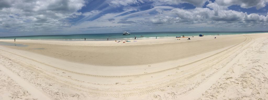 해안가 근처에 몇 사람이 있는 모래 해변, 물 위의 보트, 부분적으로 흐린 하늘.