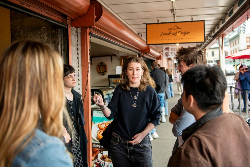 일렬로 늘어선 상점 앞 인도에 서서 대화를 나누는 한 무리의 사람들로, 한 사람이 애니메이션처럼 이야기합니다.