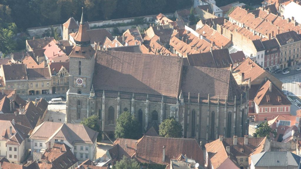 붉은 기와 지붕이 있는 촘촘하게 포장된 건물로 둘러싸인 높은 시계탑이 있는 크고 유서 깊은 교회의 공중 전망.