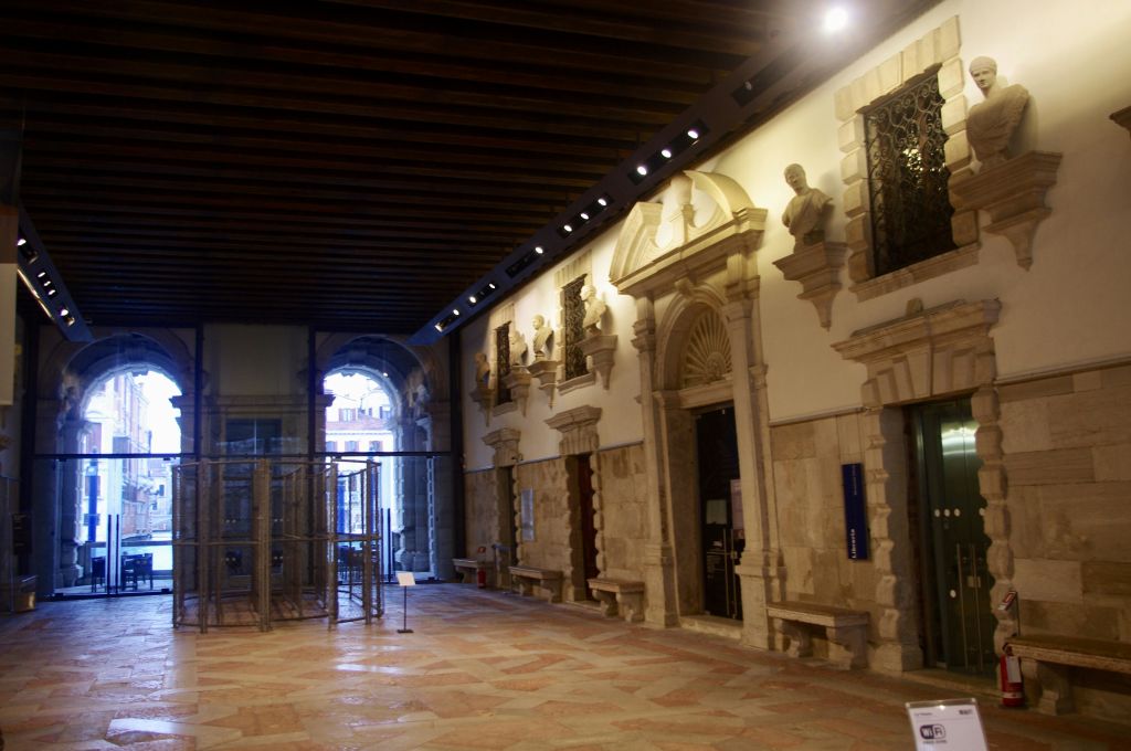 아치형 출입구, 장식용 석조 건축물, 역사적인 건물 내부의 조각상이 있는 넓은 복도.