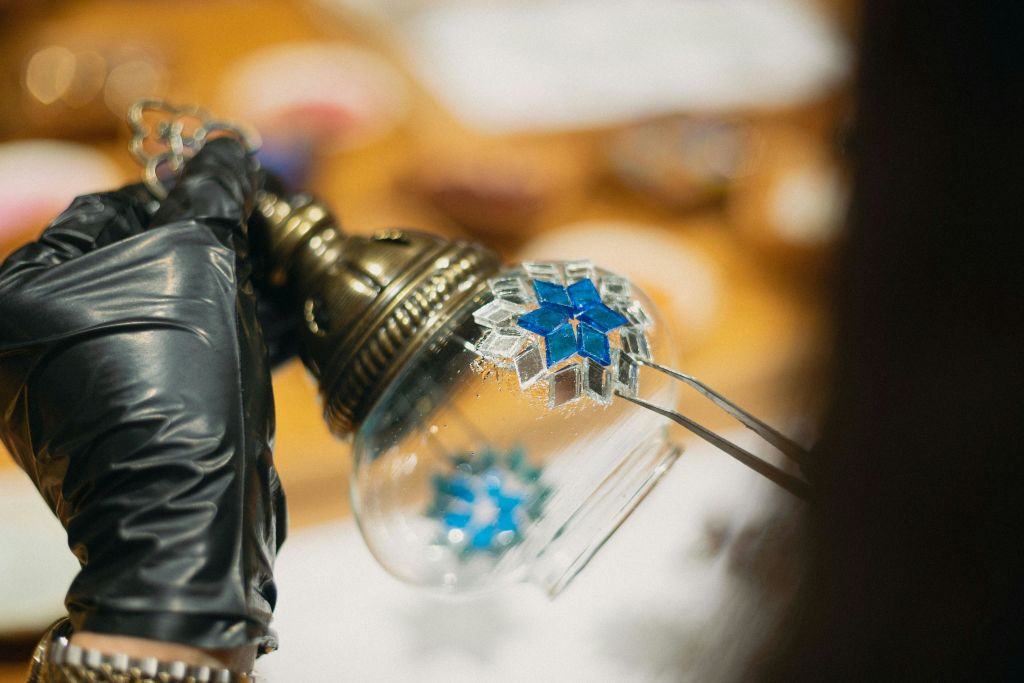 검은 장갑을 낀 사람이 유리구에 파란색 모자이크 조각을 놓은 클로즈업 사진.