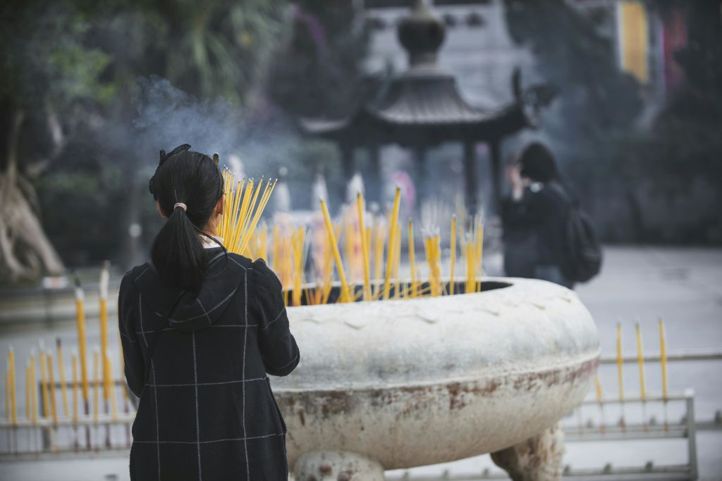 한 사람이 사원의 커다란 야외 향로에 불을 붙이고 다른 사람을 배경으로 불을 밝힙니다.