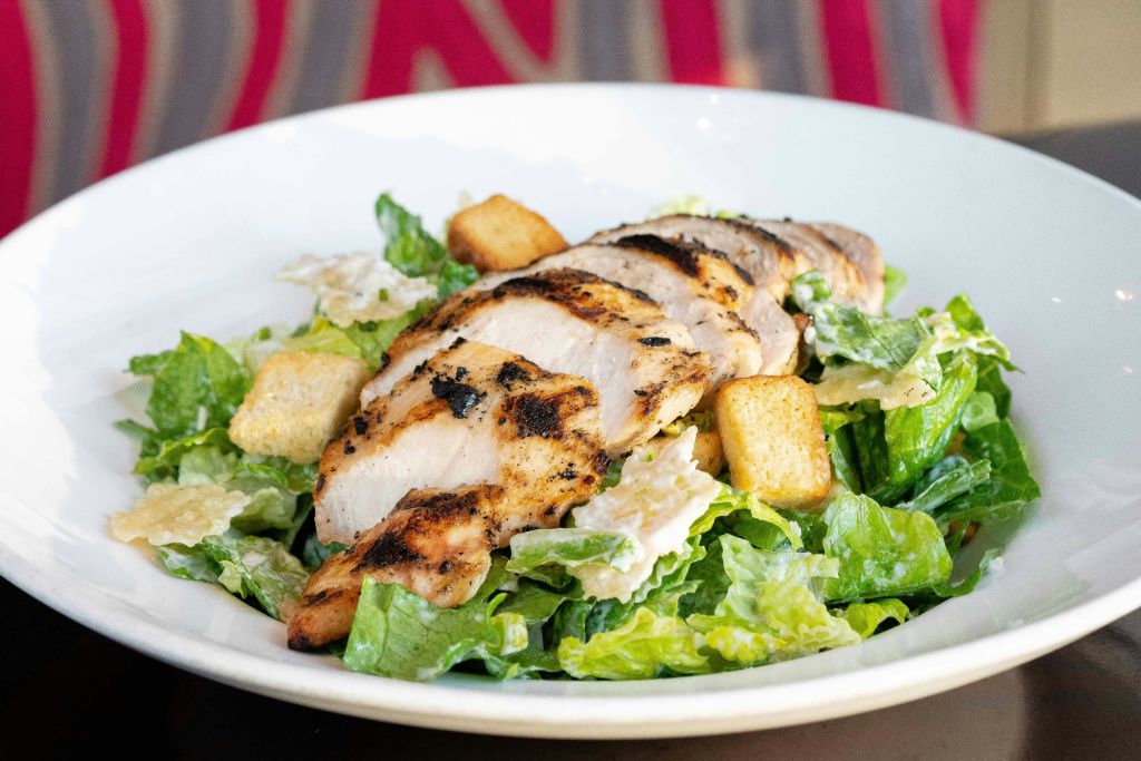 로메인 상추, 크루통, 시저 드레싱을 하얀 그릇에 담은 침대에 구운 닭가슴살.
