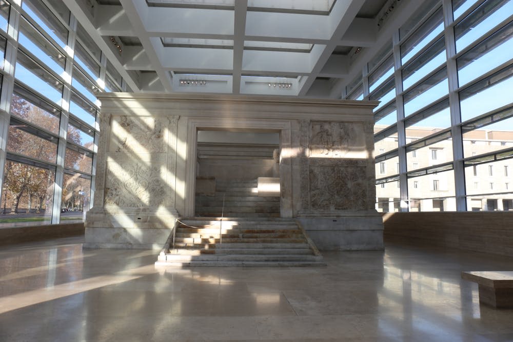 커다란 창문과 채광창이 있는 현대적인 유리 및 강철 건물에 정교한 조각이 있는 고대 석조 구조물입니다.