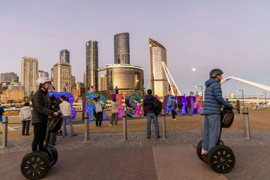 해가 질 무렵 도시의 스카이라인을 배경으로 화려한 간판 근처의 세그웨이를 걷고 타는 사람들.