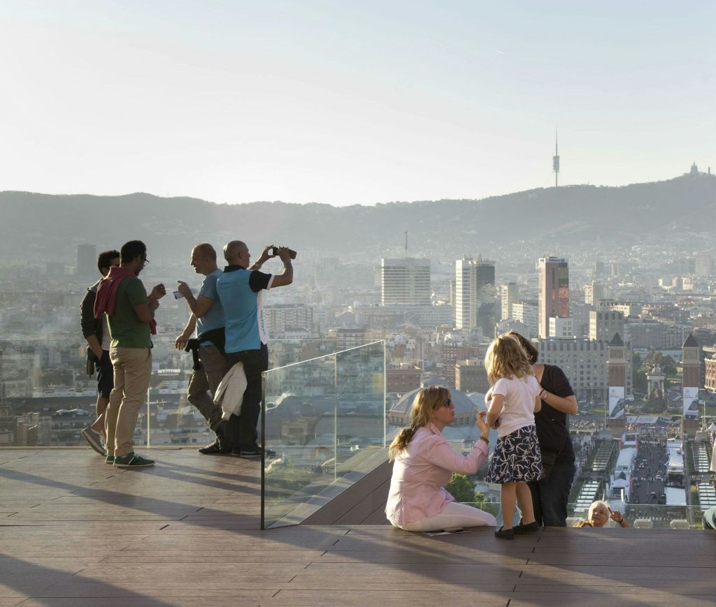 유리 난간이 있는 야외 테라스에 서서 산을 배경으로 한 도시 풍경이 내려다보이는 곳입니다.