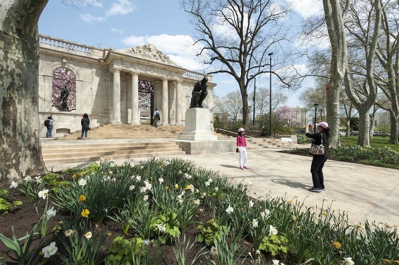 꽃과 나무로 둘러싸인 커다란 유서 깊은 건물 앞 동상 근처에서 두 사람이 사진 촬영을 위해 포즈를 취하고 있습니다.