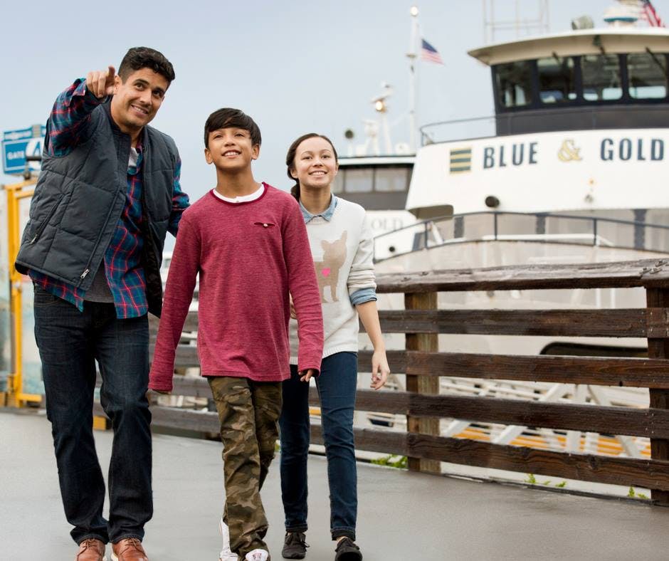 보트 근처의 선착장에서 두 명의 자녀를 둔 남성, 한 명의 자녀는 위장 바지를 입고 다른 한 명은 고양이 스웨터를 입고 있습니다.