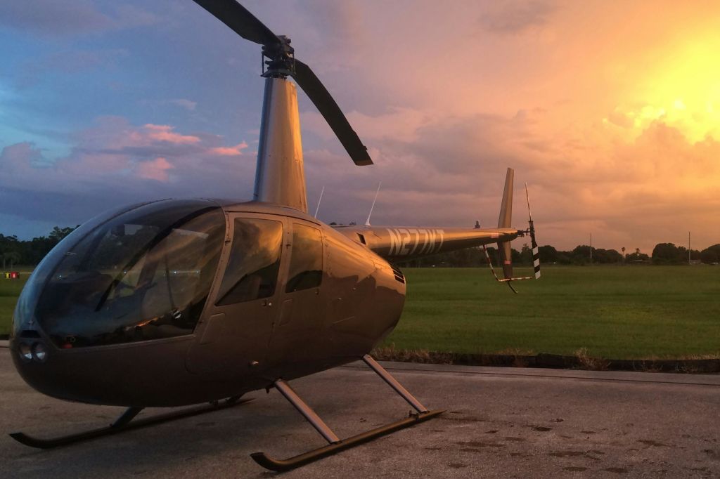 잔디밭과 활기찬 석양의 하늘을 배경으로 콘크리트 표면에 주차된 헬리콥터.