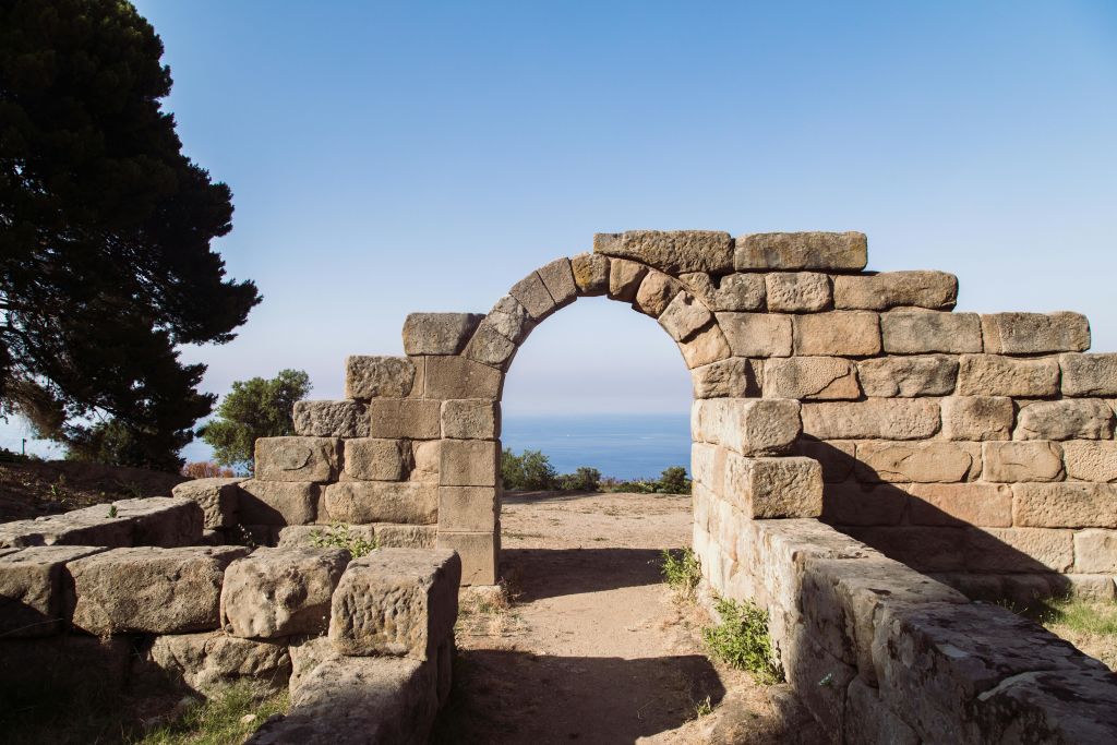 바다의 절경과 맑고 푸른 하늘을 배경으로 한 석조 아치형 유적지. 왼쪽에 나무가 보입니다.