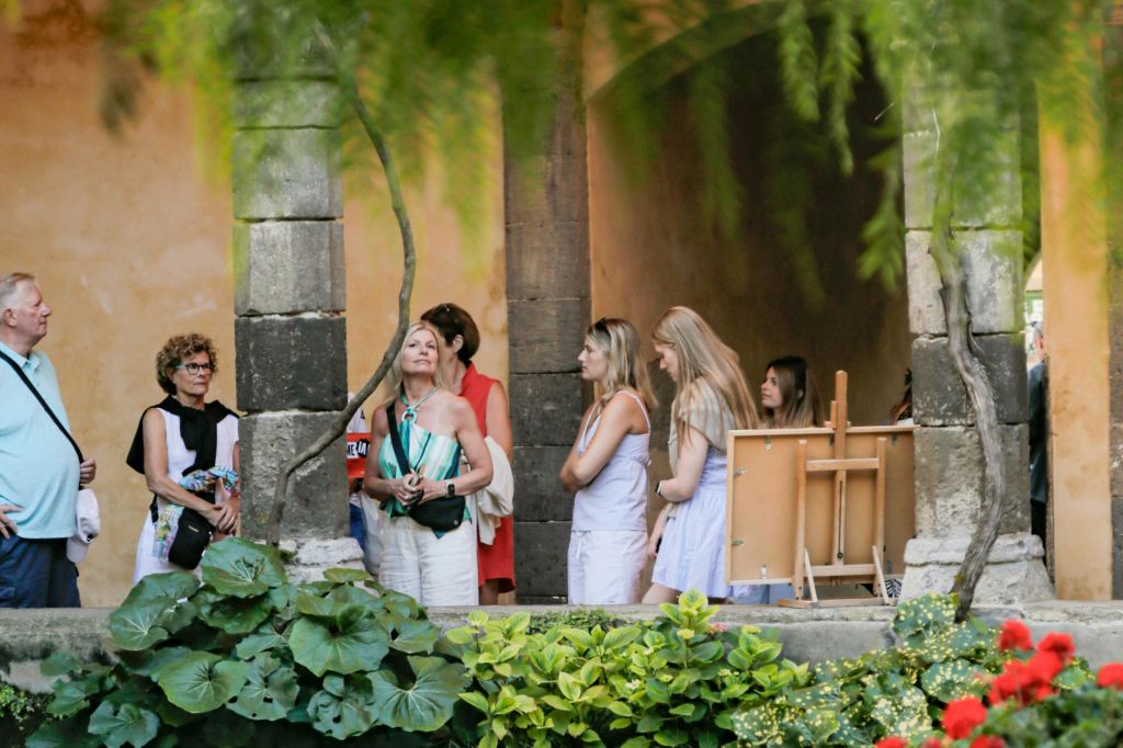 울창한 녹음과 석조 기둥이 배경으로 보이는 정원 안뜰에 서 있는 사람들.
