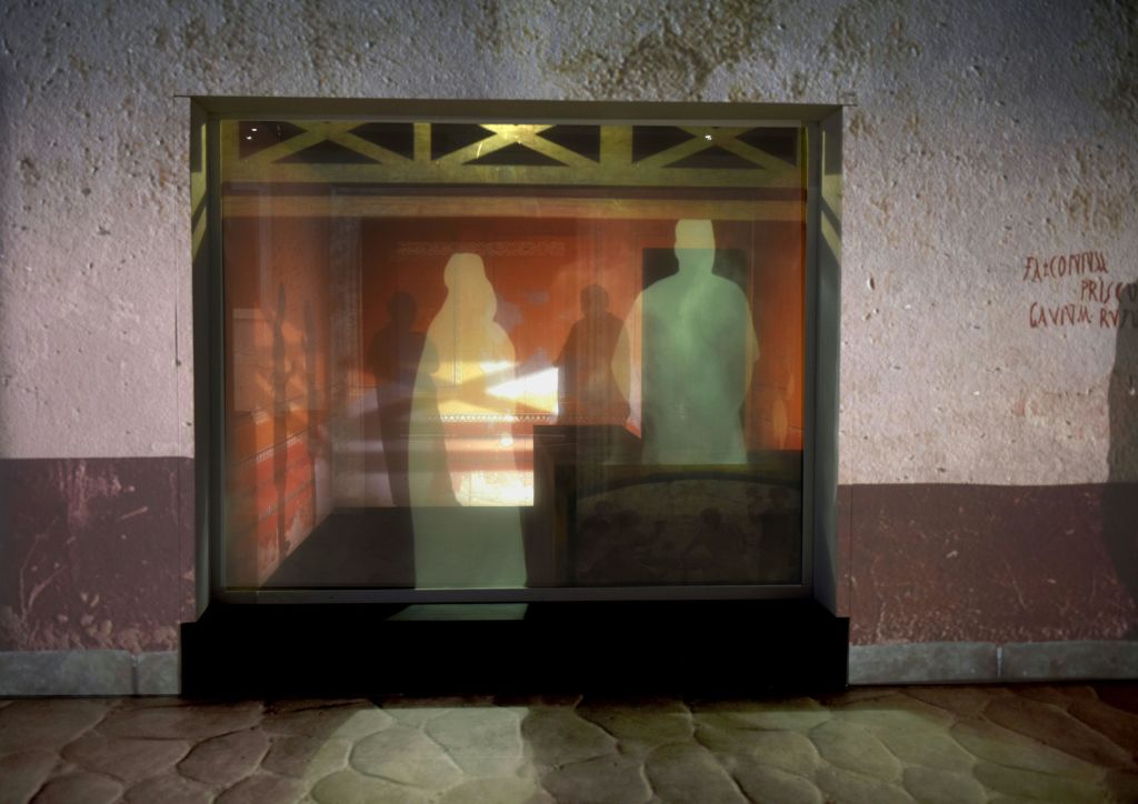 질감 있는 벽과 전경에 석조 바닥이 있는 방에 세 사람과 말 한 마리의 실루엣이 있습니다.