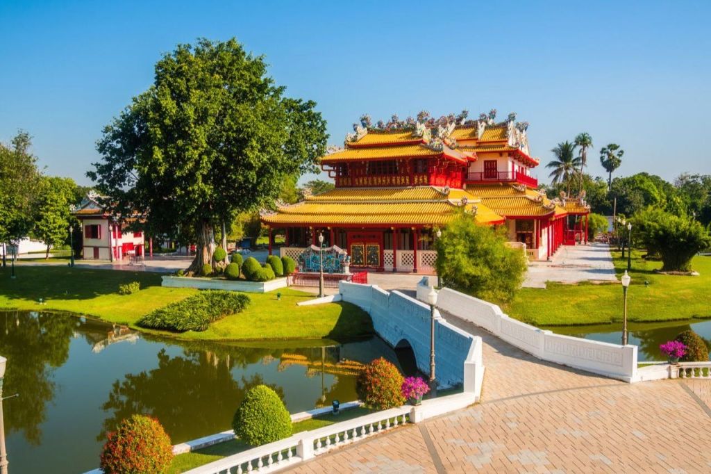 청명한 하늘 아래 조경된 정원에 화려한 디테일과 연못, 돌다리가 있는 아시아 전통 사원입니다.