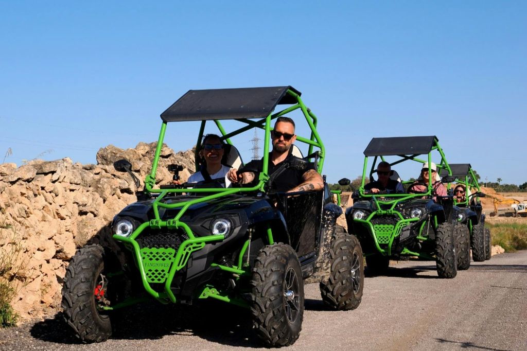 바위가 많은 지형을 배경으로 햇살이 내리쬐는 날, 녹색과 검은색의 전지형 차량을 운전하는 세 사람이 있습니다.