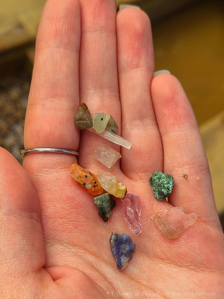 다양한 작고 화려한 크리스탈과 미네랄을 들고 있는 손. 은색 반지가 사람의 손가락에 보입니다.