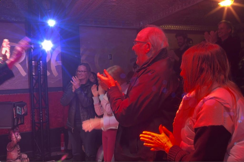 화려한 조명과 장식으로 어두운 실내 공간에서 박수를 치는 사람들의 모임.