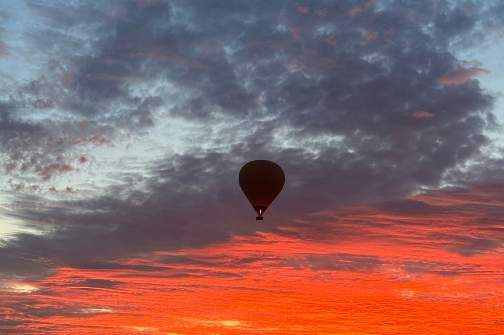 석양의 극적인 하늘을 배경으로 선명한 붉은색과 주황색 구름이 있는 열기구.