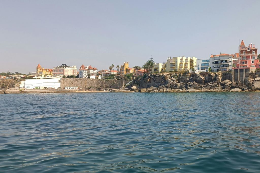 바위 해안에 화려한 건물이 있는 해안 마을로, 맑은 하늘 아래 물가에서 볼 수 있습니다.