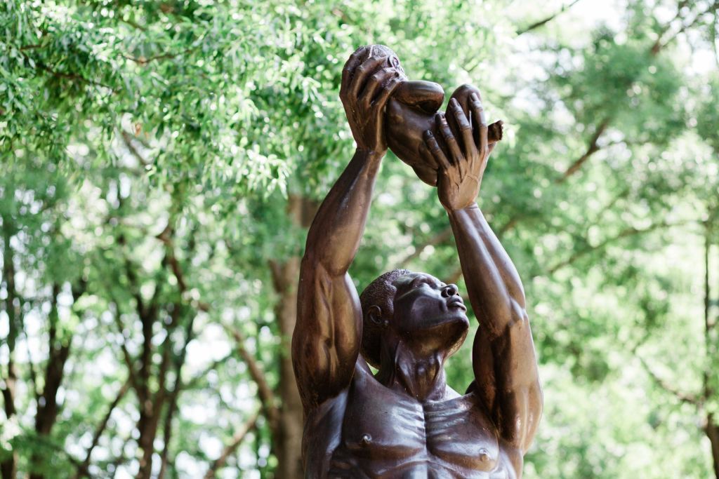 나무를 배경으로 머리 위로 아이를 안고 있는 남자의 청동 동상.