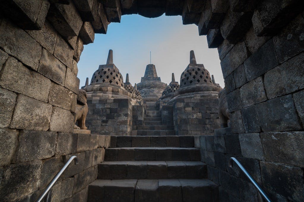 작은 스투파를 배경으로 아치형 통로가 있는 보로부두르 사원의 주요 스투파로 이어지는 석조 계단.