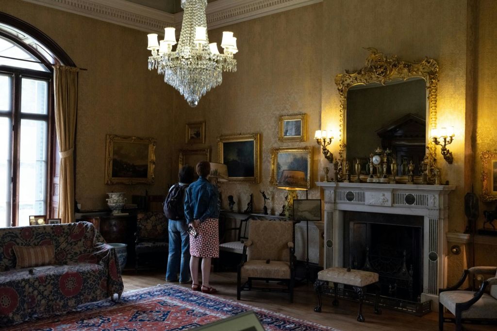 앤티크 가구, 벽에 걸린 그림, 커다란 샹들리에, 화려한 벽난로가 있는 빈티지 룸에 두 사람이 있습니다.