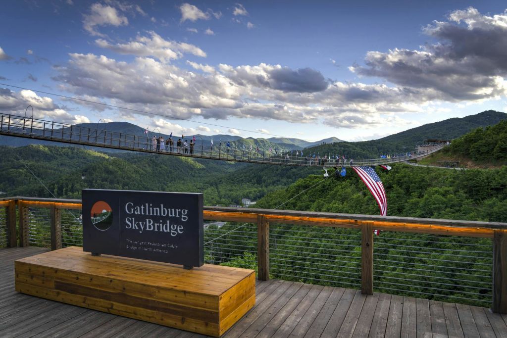 산에 있는 긴 현수교인 개틀린버그 스카이브리지 (Gatlinburg SkyBridge) 를 걷는 사람들. "Gatlinburg SkyBridge" 라는 표지판이 있습니다.