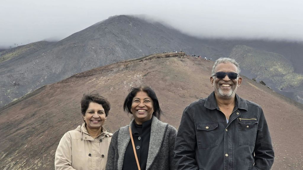 흐린 하늘 아래 안개가 낀 바위처럼 산이 많은 풍경 앞에서 세 사람이 미소를 짓고 있습니다.