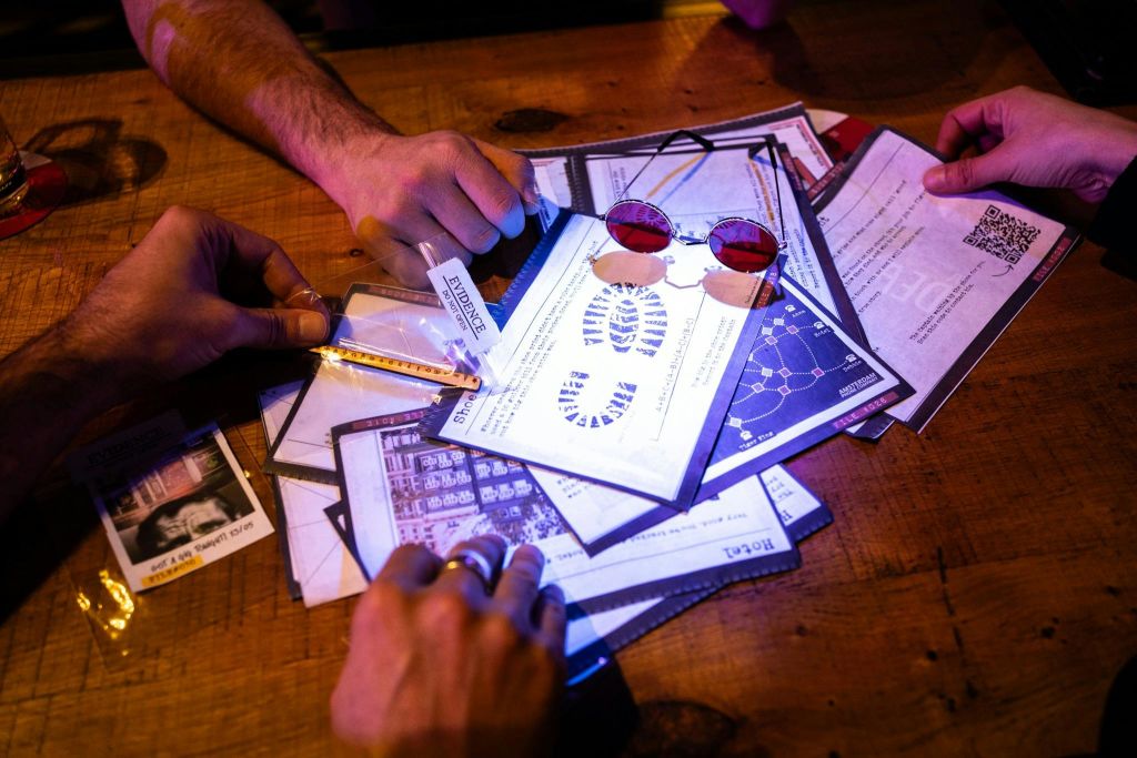 다양한 단서 시트, 유리병, 열쇠를 들고 있는 손, 나무 테이블에 과학 도표가 있는 빨간색 선글라스와 종이.