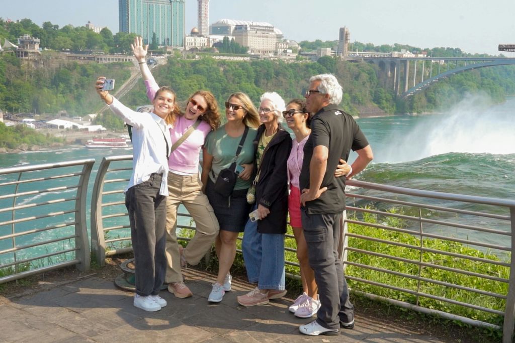 여섯 명이 도시, 나무, 물을 배경으로 아름다운 전망을 배경으로 미소를 짓고 셀카를 찍고 있습니다.