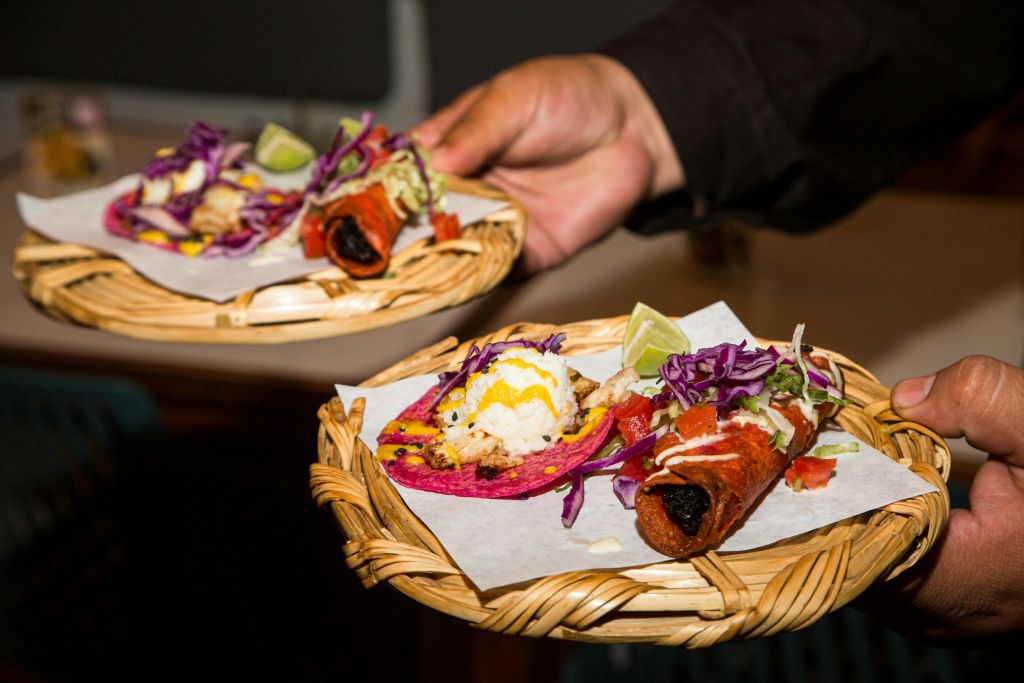 화려한 토핑과 장식이 들어 있는 도금 타코가 들어 있는 직조된 바구니 두 개를 들고 양피지에 담아 서빙하는 사람.