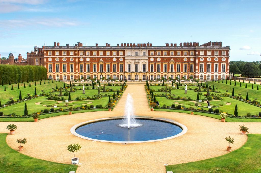 원형 분수와 잘 손질된 잔디밭이 있는 정원이 내려다보이는 수많은 창문이 있는 웅장한 붉은 벽돌 건물입니다.