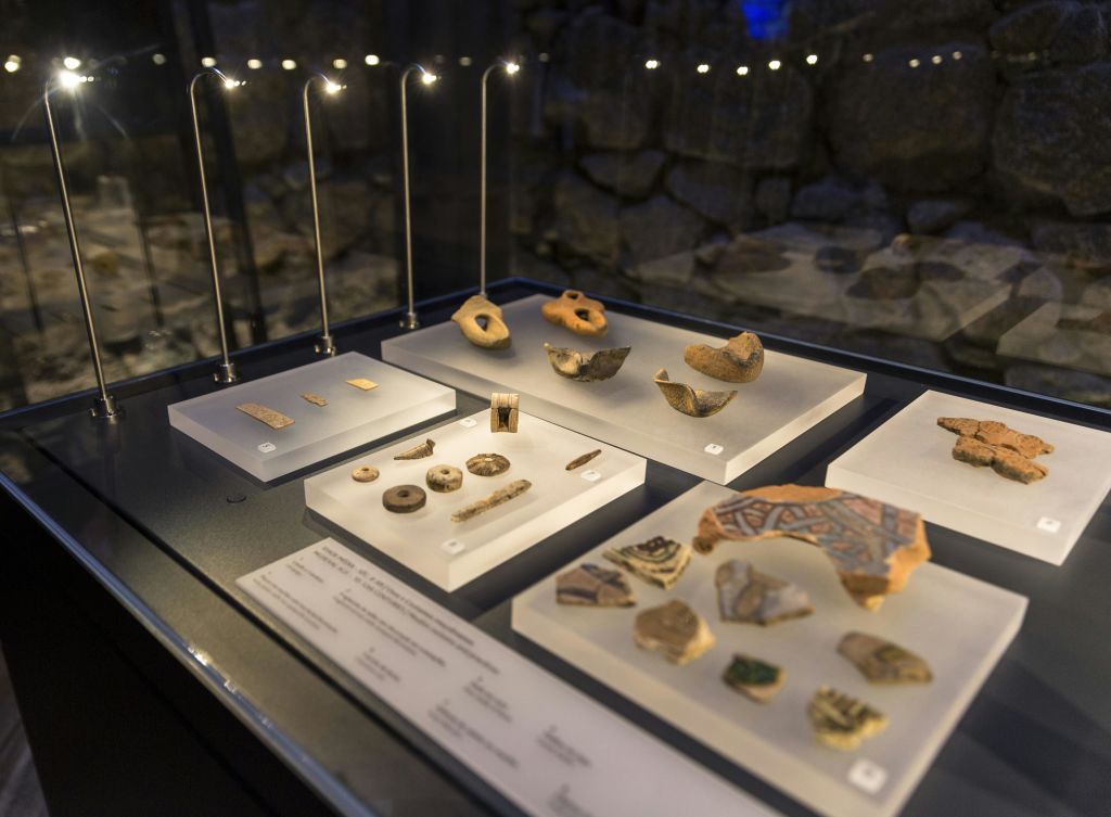 도자기 조각, 구슬 및 도구를 포함한 고고학 유물이 머리 위 조명으로 비춰진 디스플레이 케이스.