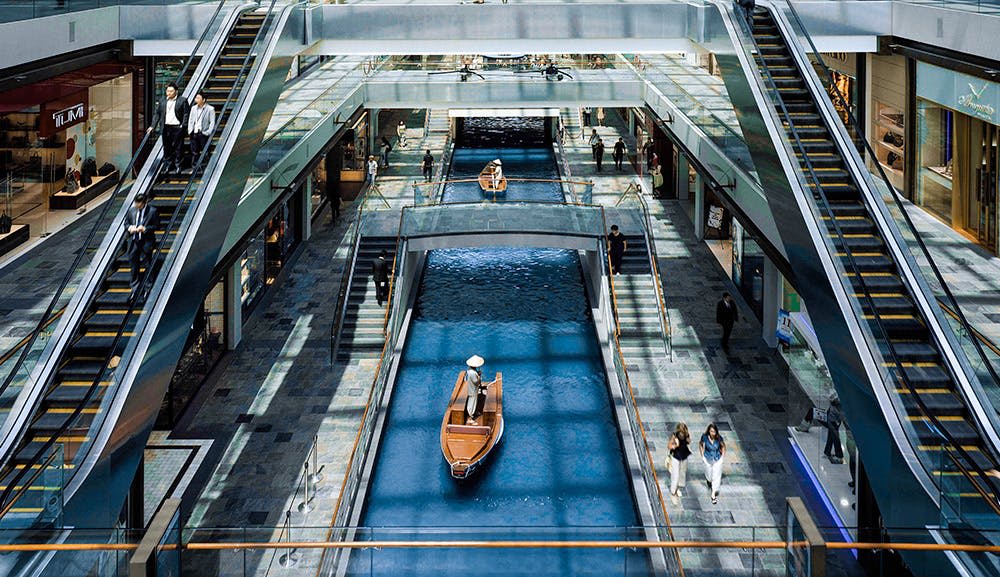 보트, 유리 난간, 양쪽에 있는 상점, 걷는 사람들이 있는 운하가 있는 쇼핑몰 인테리어.