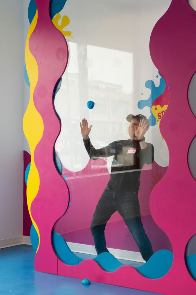 캡을 쓴 사람이 물결무늬 노란색과 분홍색으로 강조된 화려한 유리 칸막이를 눌렀습니다.